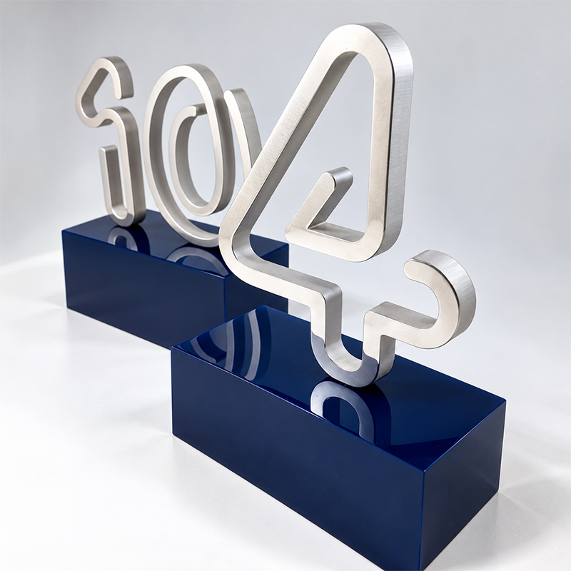 Deux trophées métalliques aux formes typographiques argentées, présentés sur des socles rectangulaires bleus brillants