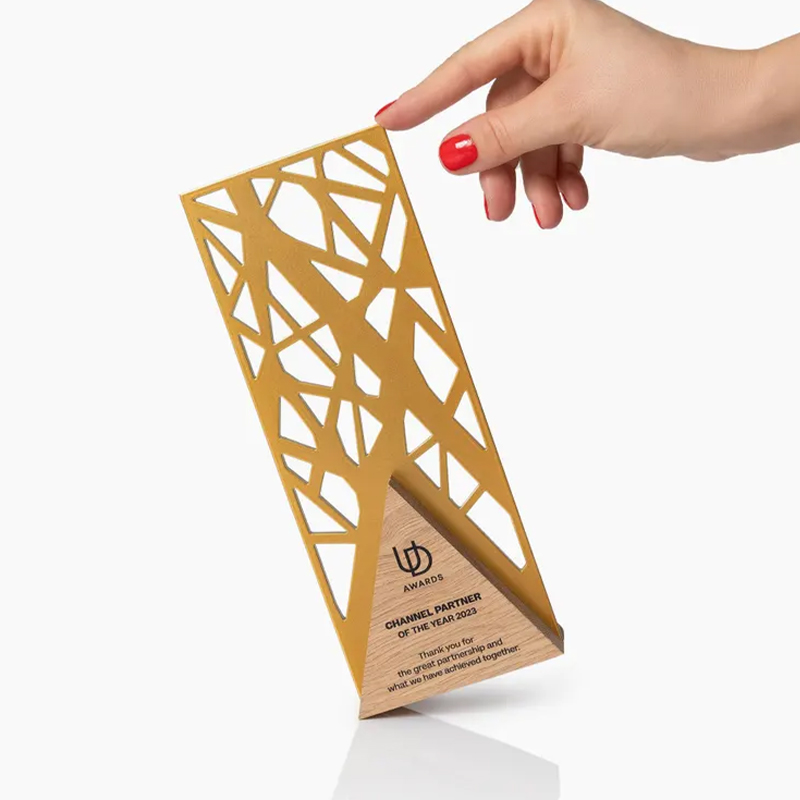 Trophée en inox avec finition effet doré, structure ajourée de motifs géométriques et support triangulaire en bois gravé UD Awards