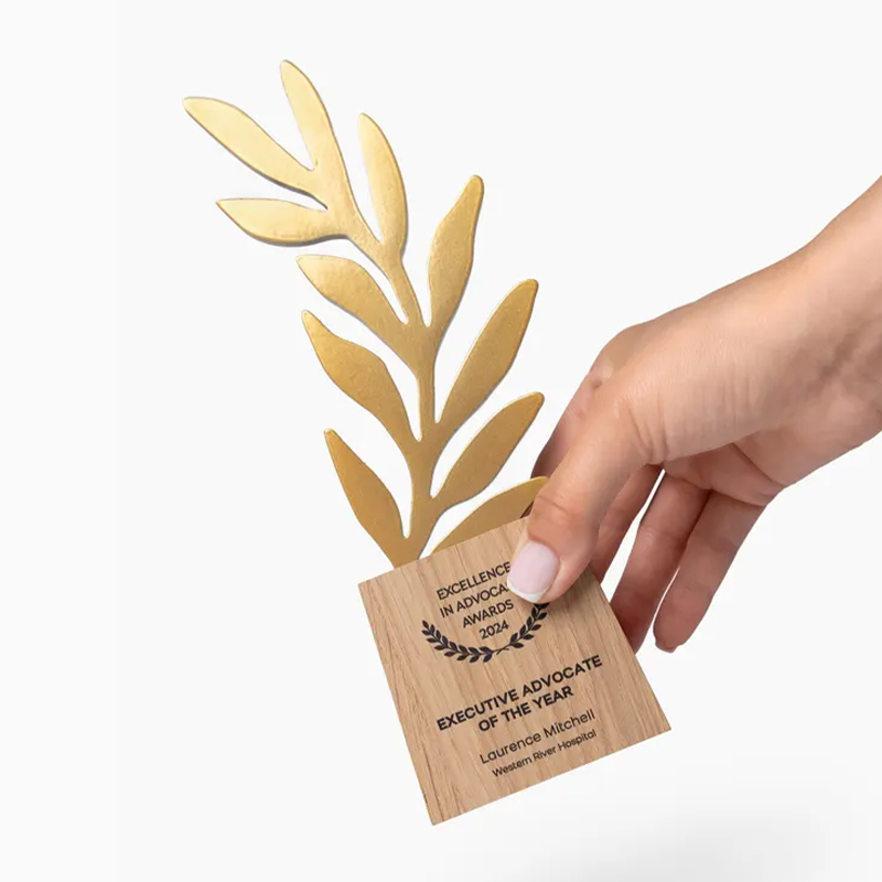Trophée en métal effet doré représentant une branche de laurier avec plusieurs feuilles, fixé sur un socle en bois gravé Excellence in Advocacy Awards 2024