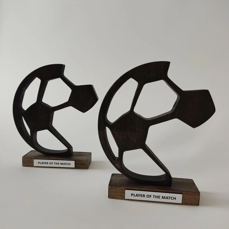 Deux trophées sportifs en métal noir avec forme découpée inspirée d'un ballon de football, montés sur des socles en bois avec inscription Player of the Match