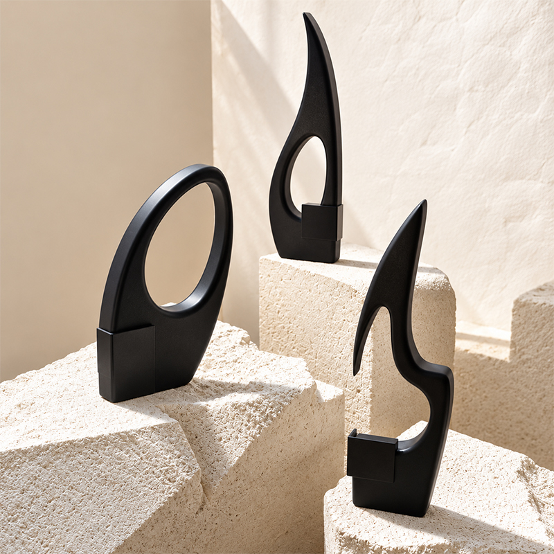 Trois trophées noirs mats aux formes abstraites ajourées, présentés sur des blocs de pierre claire